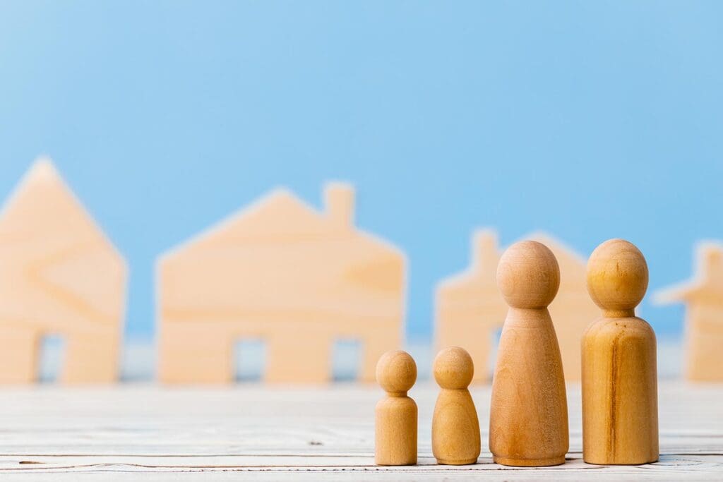 Small wooden house model and miniature wooden people figures — concept of community housing and support.